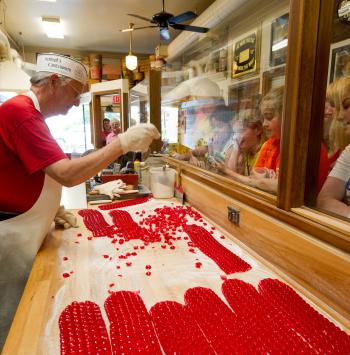 o	Schimpff's Confectionery worker displays candy making for a group of children excitedly looking on.