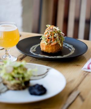 Plate of gourmet food next to glass of beer on wooden table at Wolf's Ridge Brewing