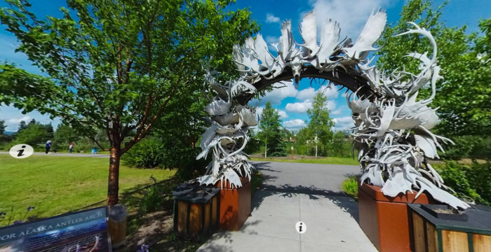 a panoramic view of an arch made of moose and caribou antlers on a park pathway in summer