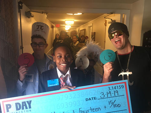 A young man holding up a check from winning the pi day recitation contest