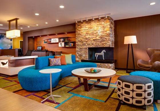 A blue curved couch in front of a faux fireplace and registration desk at the Fairfield Inn in Elkhart