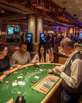 Three people sit at a blackjack table in a casino as a dealer hands out cards.