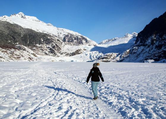 A person hiking along the frozen Mendenhall Lake surrounded by mountains.