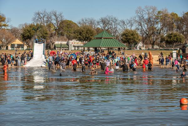 A group of people run into the lake and one person slides down a snow hill into the lake