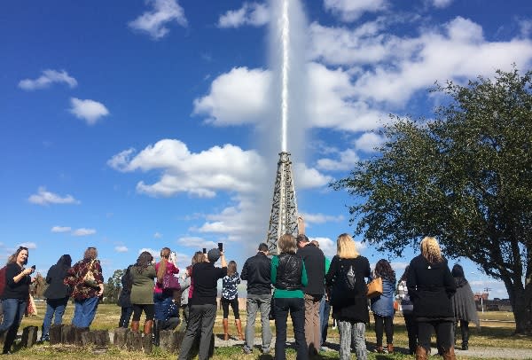 Visitors watch the gusher blow against a blue sky
