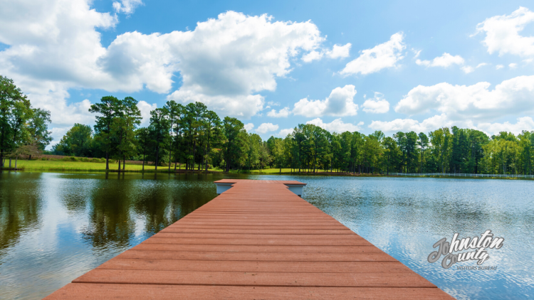 A dock that leads off into a lake with sun and blue sky