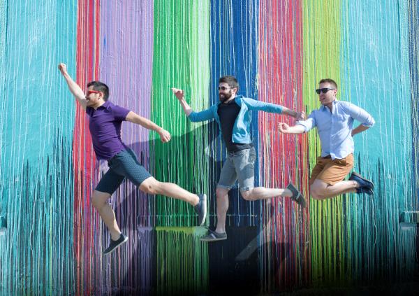 Three men posing in front of the Biscuit Paint Wall