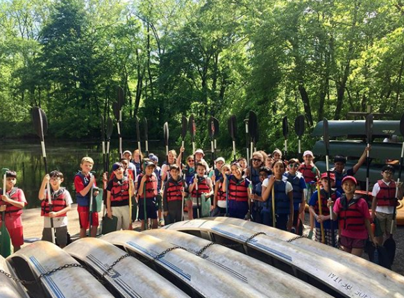 A group of children wearing life jackets standing by kayaks i Princeton