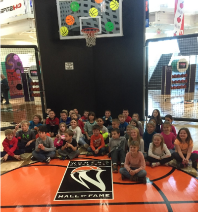 A group of children sit on a basketball court at the Women's Basketball Hall of Fame in Knoxville, TN