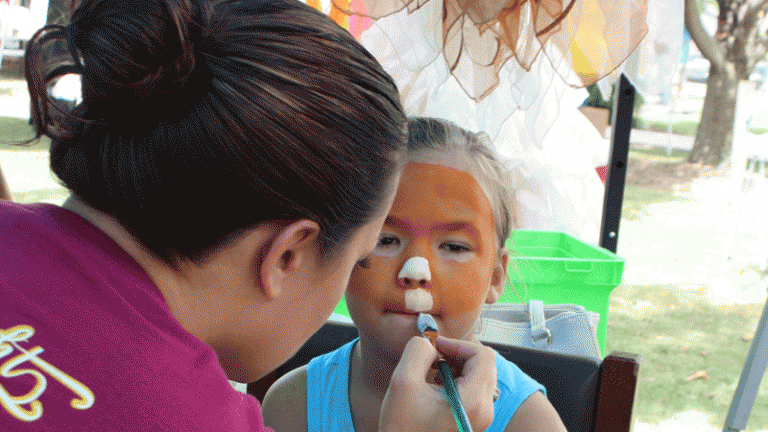 A young girl getting her face painted orange and white at the Red Bay's Founder Fest