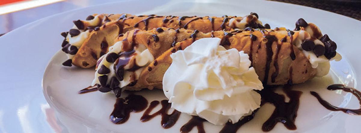 Cannoli with whipped cream, chocolate chips and chocolate drizzle on a white plate