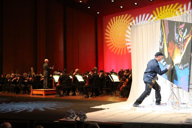 An artist paints on canvas in accordance with the Wichita Symphony Orchestra that plays behind him