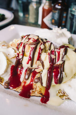 A banana Nutella crepe on a plate with chocolate sauce and berry sauce