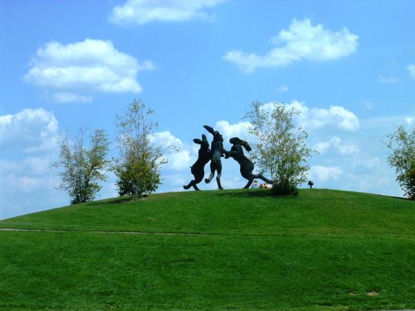 Three giant rabbit sculptures at the top of a grassy hill.