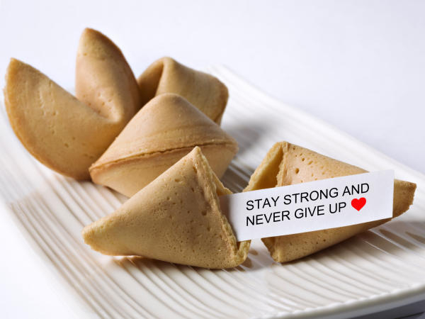 A handful of fortune cookies sit on a tray, with one cracked open and the fortune delivering encouraging words.