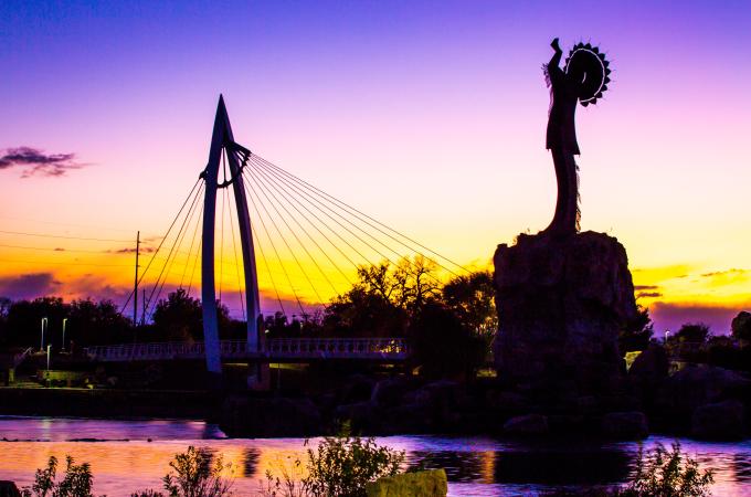 The sun sets behind the Keeper of the Plains with a purple and yellow sky