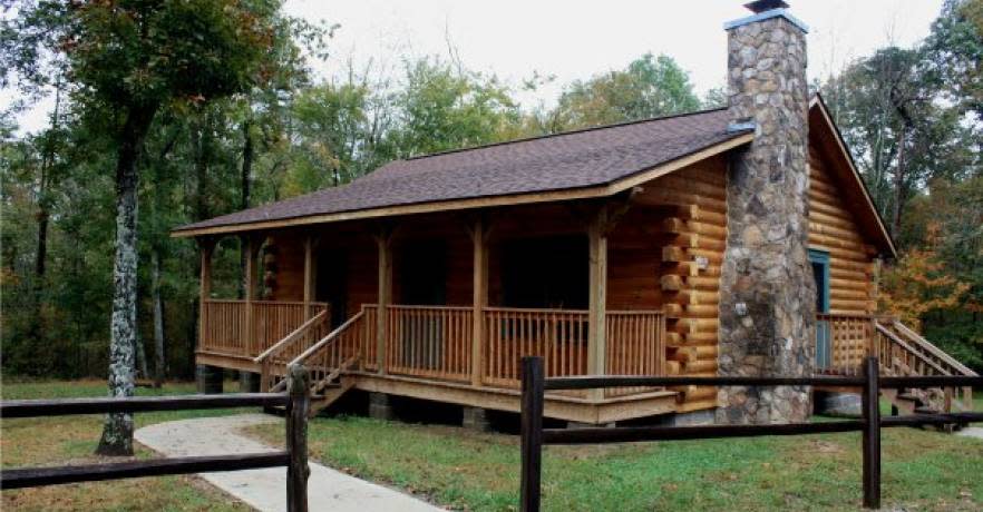 The front of a log cabin with a stone chimney on the side.