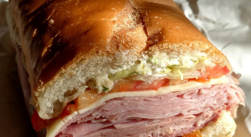Close up of a sub sandwhich stacked with meat cuts, lettuce, tomato, and provolone between crispy Italian bread.