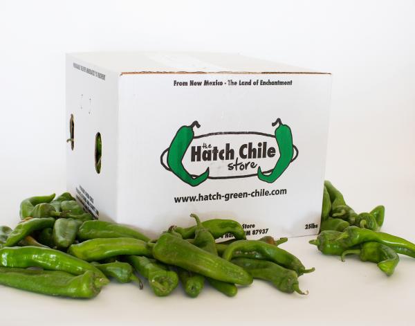 A box with The Hatch Chile Store logo and a pile of fresh green chiles around it