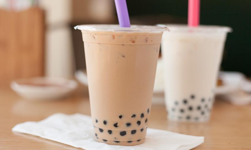 Two Boba drinks with purple and pink straws on a table