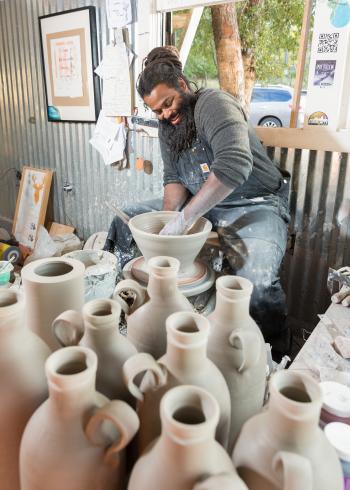 Man working at wheel in studio surrounded by clay jars at Ro Shaw clay studio in salado texas