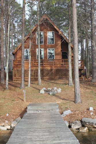 An A-frame cabin surrounded by trees near the water.