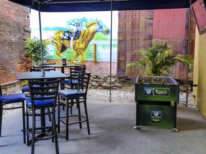 Black patio seating infront of thoroughbred horse racing decal on brick wall at Peabody's patio in Saratoga Springs NY