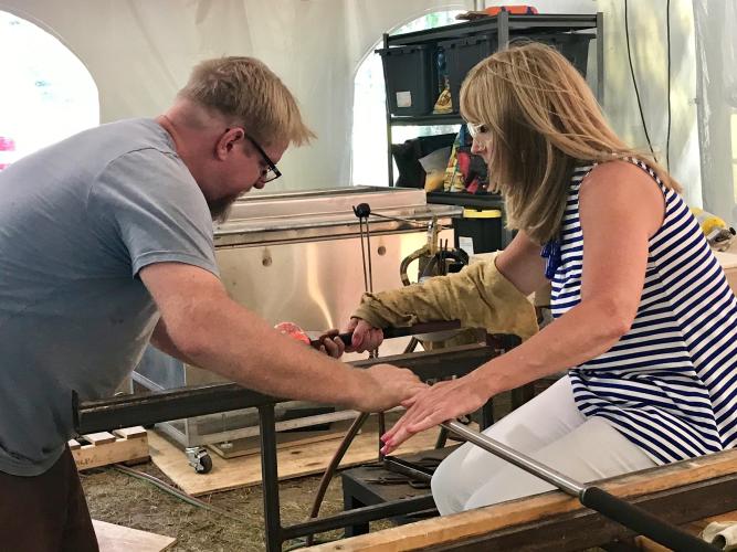 Gail sitting at the work bench and spinning the tube while Greg leans over toward her to help