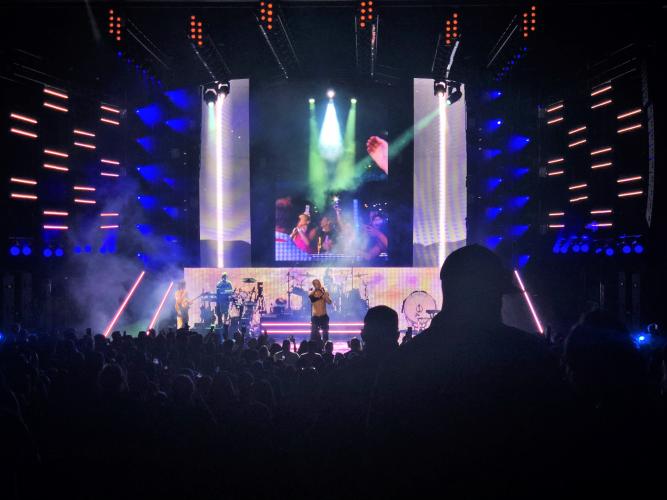 A band performing on stage at SPAC with laser lighting and backdrop of purple lights