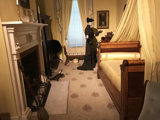 Walworth Mansion bedroom exhibit with woman standing by bed in yellow room with large fireplace