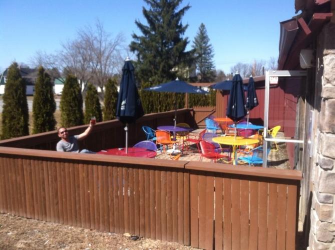Picture of guy holding up a beer with colorful tables and chairs at King Tavern's patio