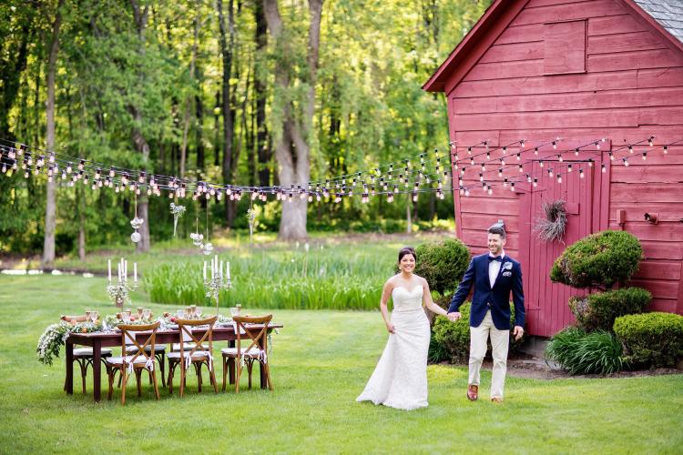 Damaranville Farm and Garden bride and groom holding hands in daylight and standing by red barn with tiny lights strung overhead
