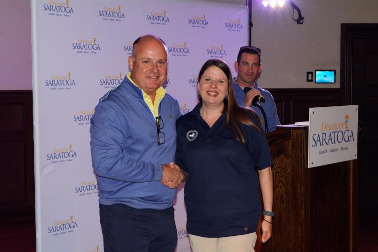 Darryl shaking female golf award winner's hand in front of the Discover Saratoga backdrop
