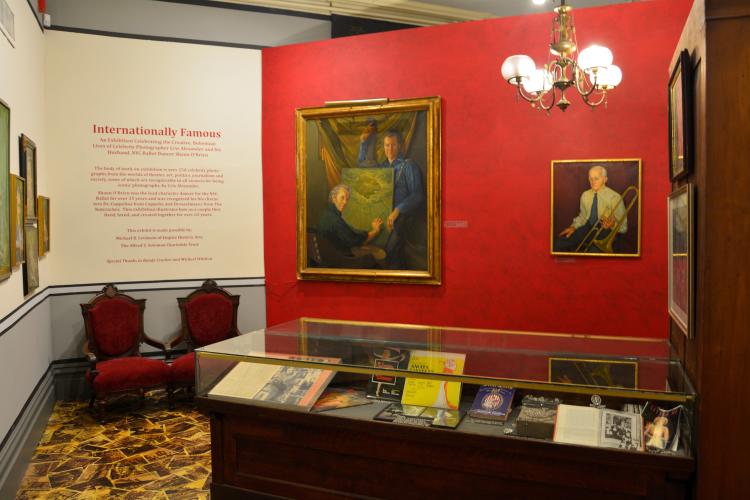 Internationally Famous exhibit wall, red with portraits hanging and a display case in front of it
