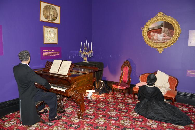 Mourning Room with man playing piano and woman kneeling by couch under portrait of Walworth baby