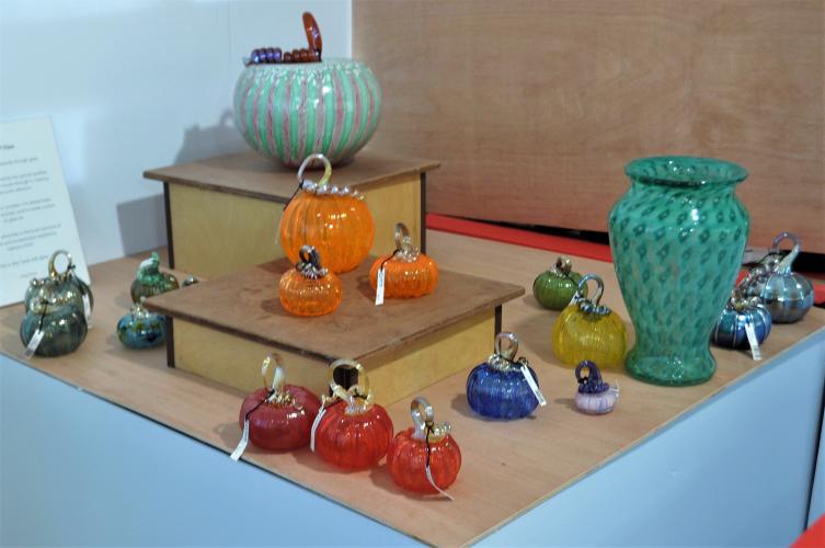 Glass works gallergy Greg Tomb with examples of a vase, bowl and several pumpkins in many colors