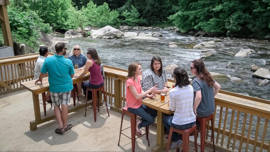 Diners enjoy happy hour on the riverside patio at Hickory Nut Brewery in Chimney Rock, NC.
