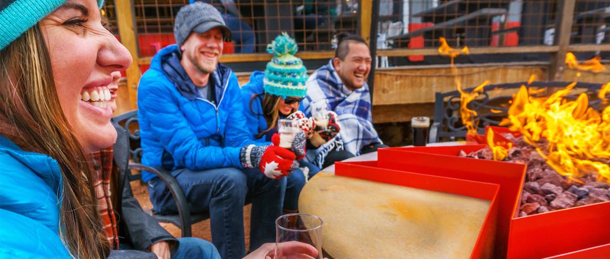 Two men and women laughing around a firepit at Sanitas Brewery