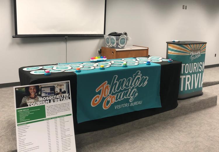 A table set with tourism industry information and gifts sits on a raised platform in a classroom.