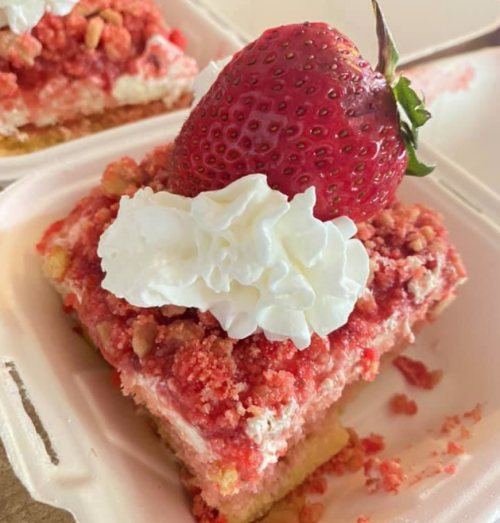 A fresh strawberry sits atop a dollop of cream on a slice of Ruby's Delights' strawberry shortcake.