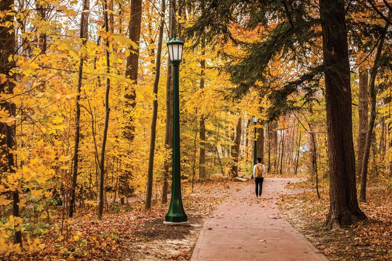 IU student walking with a backpack on a path in Dunn Woods during the fall