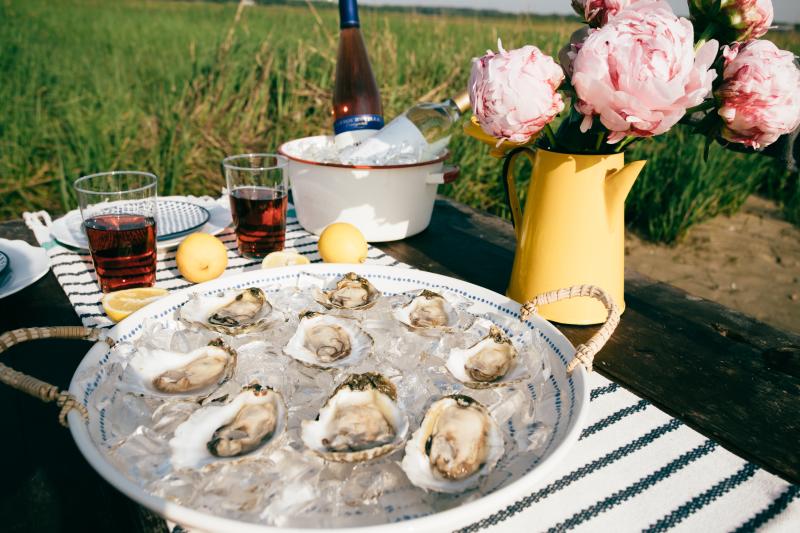 Oysters on the half shelf in a bowl of ice with wine and flowers on a table for the Pleasure House Oyster Boat Tour