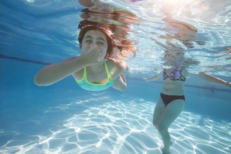 Valley River Inn pool by Turell Group A child holds her breath under water in a large swimming pool. Her mom is behind her wading in.