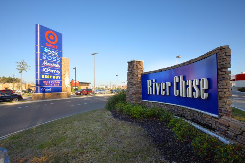 The entrance of River Chase shopping center marked by a blue sign listing various stores in a variety of colors