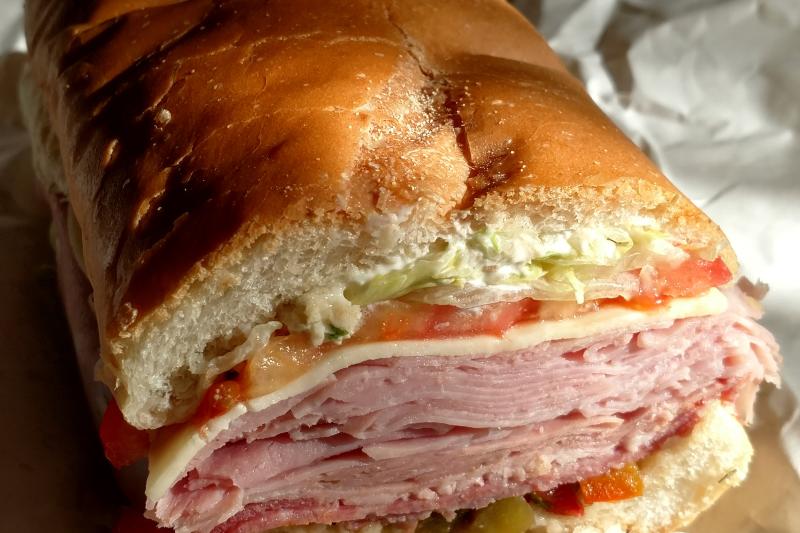 Close up of a sub sandwich stacked with meat cuts, lettuce, tomato, and provolone between crispy Italian bread.