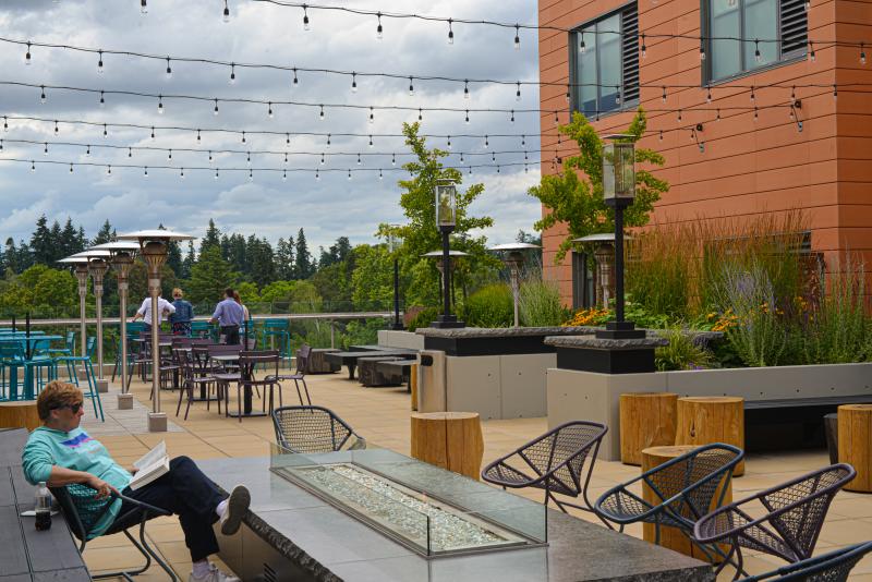 Hyatt Place at Oakway Center SkyDeck Lounge by Melanie Griffin Person reads beside the fire pit on the sky deck lounge at Hyatt Place in Eugene. There are string lights, tables and people in suits drinking on the ledge in the distance.