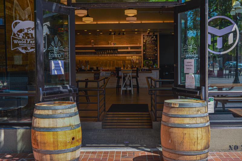 Manifest Brewing by Melanie Griffin Two wine barrels sit in front of open doors leading into a clean looking taproom at Manifest Brewing.
