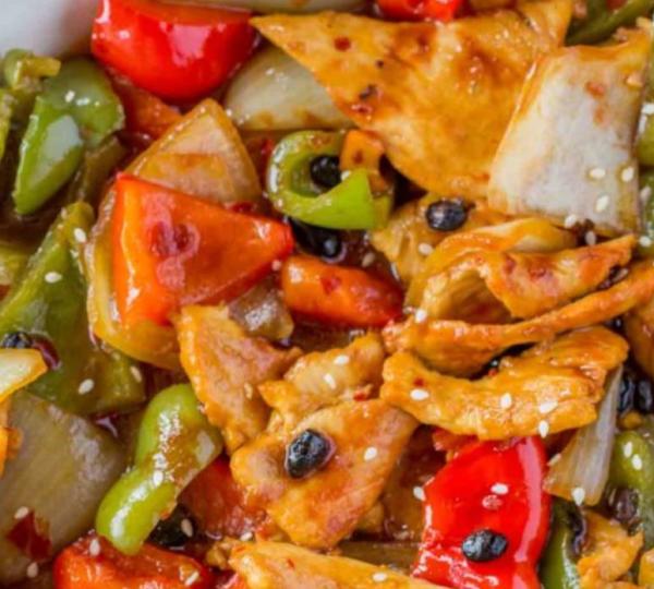 A dish of black bean chicken is mixed with red and green bell peppers.