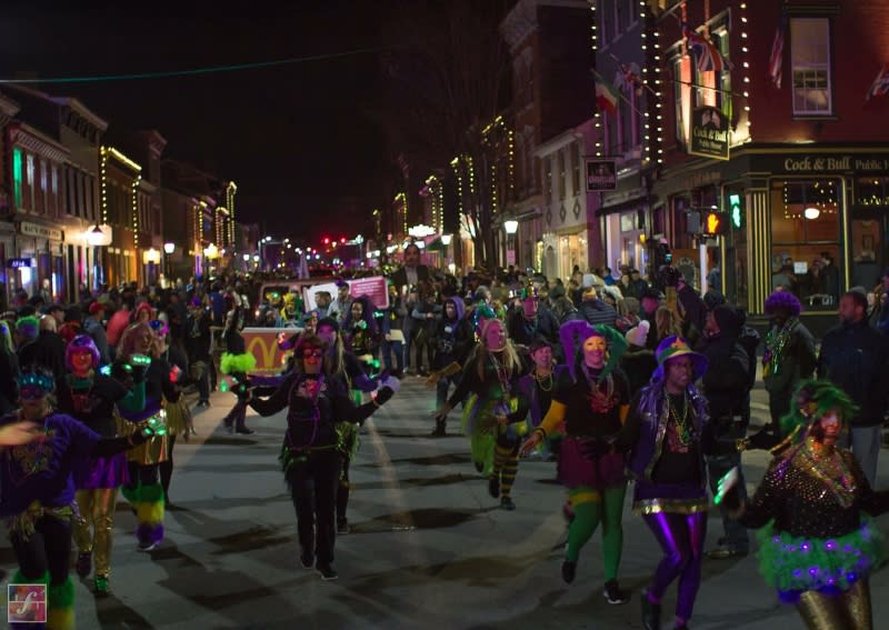 People dressed in green, purple and gold holding lights and marching in Mainstrasse Village's mardi gras parade at night.