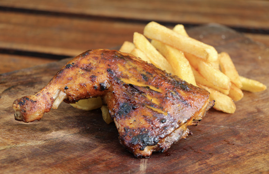 A grilled piece of chicken beside French fries on a wooden table